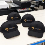 כובעי מצחייה שחורים ממותגים בלוגו SYNCRO צבעוני – דוגמת עבודה