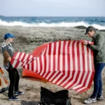 מחצלת חוף משפחתית ממותגת – שני אנשים פורסים מחצלת אדומה־לבנה בקמפינג
